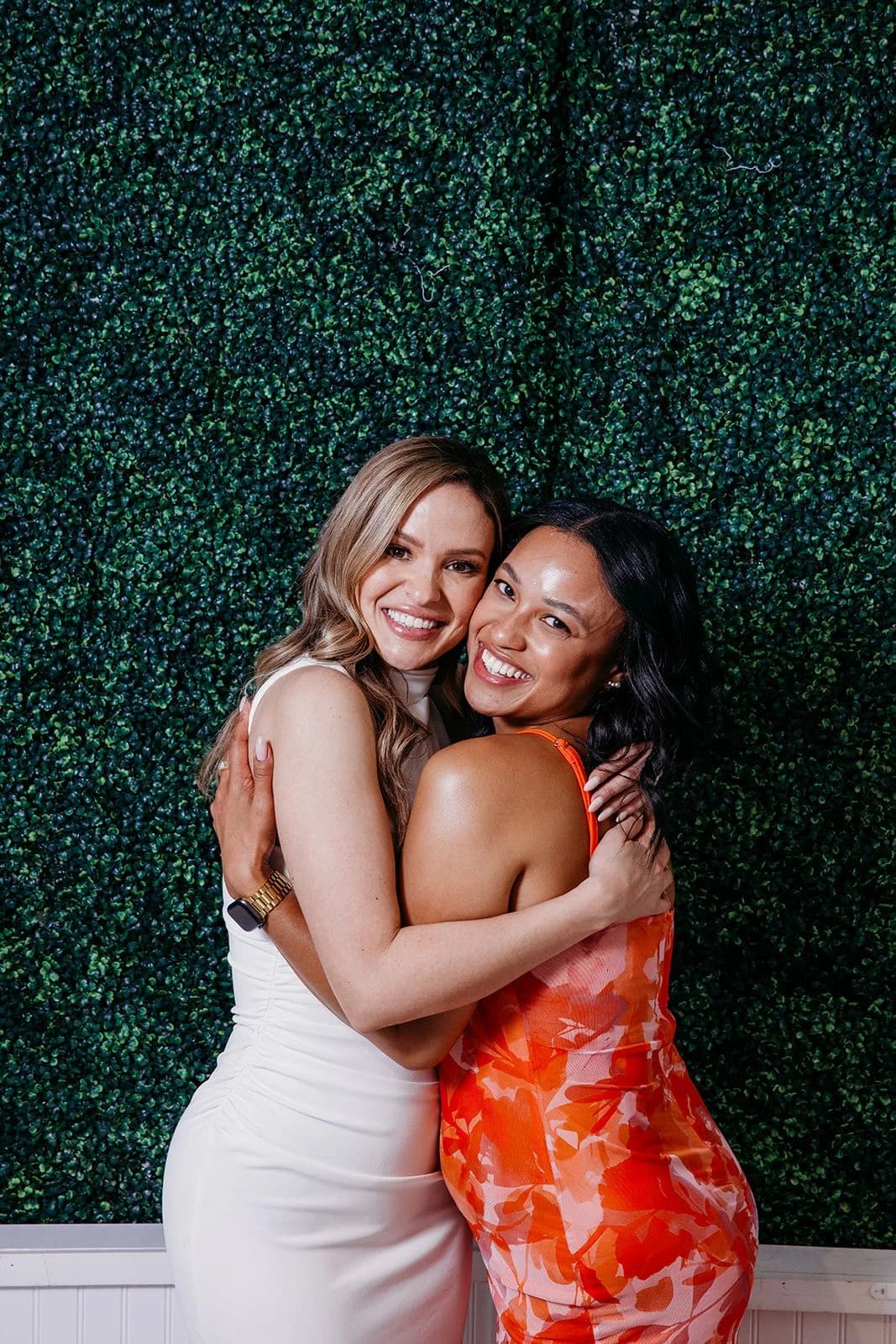 Two guests celebrating beside the greenery wall at Gather.